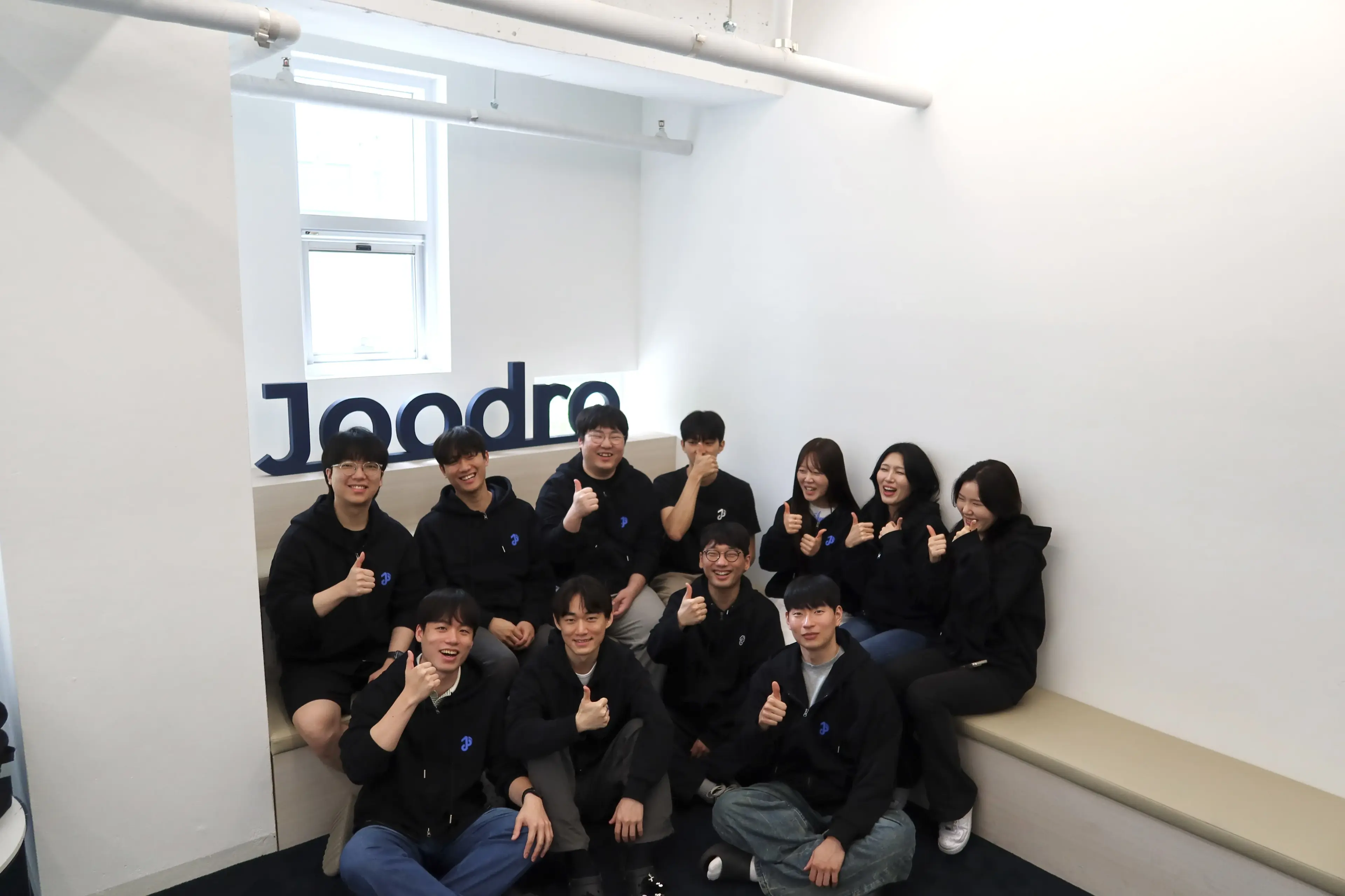 오피스의 Joodra 사인 앞에 모인 팀 전체